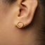 A close-up view of a person's ear, showing a gold hoop earring with a circular shape.