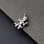 A silver-colored metal charm or brooch in the shape of a voodoo doll is resting on a textured gray surface.