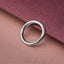 A silver ring is resting on a textured pink background.