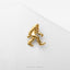 A gold-colored metal pin or brooch in the shape of a human figure, possibly a Sasquatch, is shown against a white background.