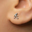 A close-up of a person's ear with a small silver earring featuring a figure of a person.