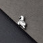A small silver-colored metal object resembling a horse or a similar animal shape is placed on a textured gray surface.