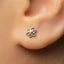A close-up of a person's ear with a small, silver earring featuring a star-like design.