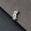 A small, silver-colored metal object, possibly a piece of jewelry, is resting on a textured gray surface.