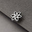 A silver-colored metal pin or bangle with an intricate star-shaped design, resting on a textured gray surface.