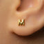 A close-up of a person's ear with a small gold letter earring featuring the letter 'M' in the center.