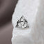 A silver-colored metal earring in the shape of a triangle is resting on a white surface.