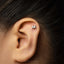 A close-up of a person's ear with a small letter "M" stud earring in the earlobe.