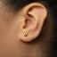 A close-up of a person's ear with a small gold letter earring featuring the letter 'M' in the center.