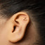 A gold-colored earring with a small hanger-shaped design is visible in the ear of a person.