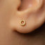 A close-up view of a person's ear with a small gold-colored earring in the earlobe.