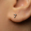 A close-up of a person's ear with a small silver earring featuring the number 7.