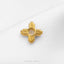 A gold-colored metal piece with a cross-shaped design is displayed on a white fabric surface.