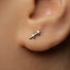 A close-up of a person's ear with a small silver earring featuring a symbol, likely an astrological sign, attached to the earlobe.