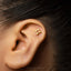 A close-up of a person's ear with a small gold-colored earring in the earlobe.