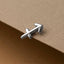 A silver earring in the shape of the Sagittarius zodiac sign is resting on a brown surface.