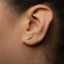 A close-up of a person's ear with a small silver earring featuring a symbol, likely an astrological sign, attached to the earlobe.
