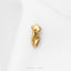 A small gold-colored pin or brooch is resting on a white fabric surface.