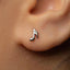 A close-up view of a person's ear with a small silver earring featuring a musical note design.