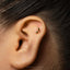 A close-up of a person's ear with a small gold earring featuring a musical note design.