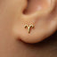 A close-up of a person's ear with a small gold-colored earring featuring a symbol resembling a zodiac sign.