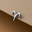 A silver earring in the shape of a zodiac sign, specifically a Leo, is resting on a brown surface.