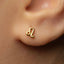 A close-up of a person's ear with a small gold earring featuring a symbol, likely an astrological sign, in the earlobe.