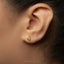 A close-up of a person's ear with a small gold earring featuring a symbol, likely an astrological sign, in the earlobe.
