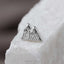 A silver earring in the shape of a mountain peak is resting on a white surface.