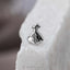 A small silver earring in the shape of a bag with a dollar sign on it, placed on a white surface.