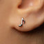 A close-up view of a person's ear with a small silver earring featuring a musical note design.