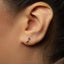 A close-up view of a person's ear with a small silver earring featuring a musical note design.