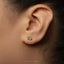 A close-up of a person's ear with a small silver earring featuring the astrological sign symbol for Capricorn.