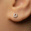 A close-up of a person's ear with a small silver earring featuring the letter 'D' in the shape of a letter.