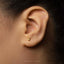 A close-up of a person's ear with a small gold earring in the earlobe.