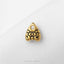 A small gold-colored charm with an eye design is placed on a white surface.