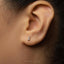 A close-up of a person's ear with a small silver letter "J" earring in the earlobe.