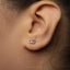 A close-up view of a person's ear with a small silver earring featuring a pair of interlocking rings.
