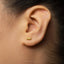 A close-up of a person's ear with a small gold earring in the earlobe.