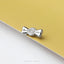 A silver-colored metal pin or charm in the shape of a candy wrapper is resting on a yellow surface.