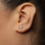 A close-up of a person's ear with a small silver earring featuring a bow design.