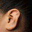 A close-up of a person's ear with a gold earring featuring a zodiac symbol in the earlobe.