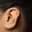 A gold-colored earring with an Egyptian hieroglyphic symbol is visible in the image.