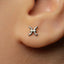 A close-up of a person's ear with a small silver earring featuring a zodiac symbol in the earlobe.