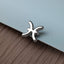 A silver metal pin or clip with a zodiac symbol design is resting on a textured surface.