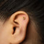 A close-up of a person's ear with a small gold earring featuring the number 8 on it.