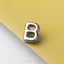 A shiny metal letter 'B' is placed on a yellow surface.