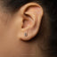 A close-up of a person's ear with a small silver earring featuring the number 8 on it.