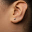 A close-up of a person's ear with a small silver letter 'H' stud earring.