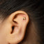 A close-up of a person's ear with a small gold letter "N" stud in the earlobe.